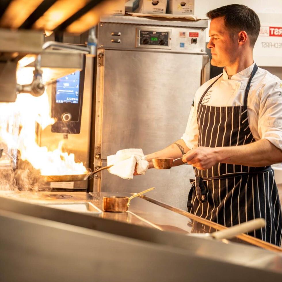 A chef holding a pan with flames coming off of it